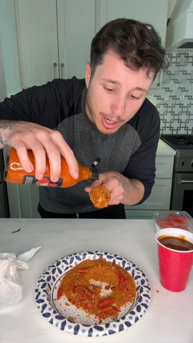 a man is pouring sauce on a plate with food and drink in front of him