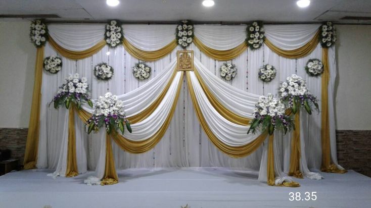 the stage is decorated with white flowers and gold drapes