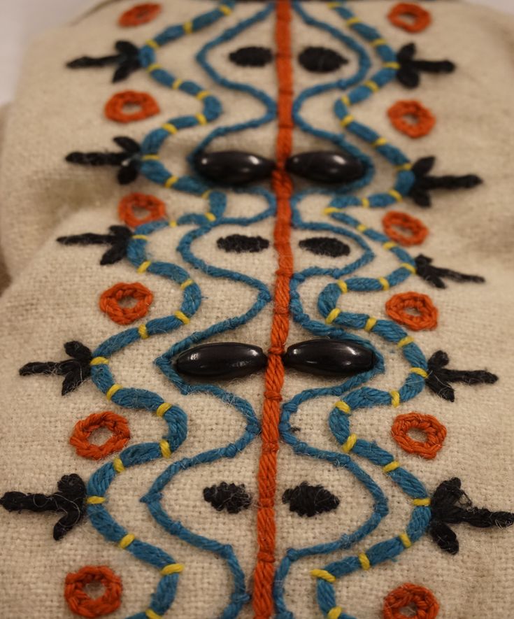 a close up of an embroidered object on a white surface with orange and blue lines