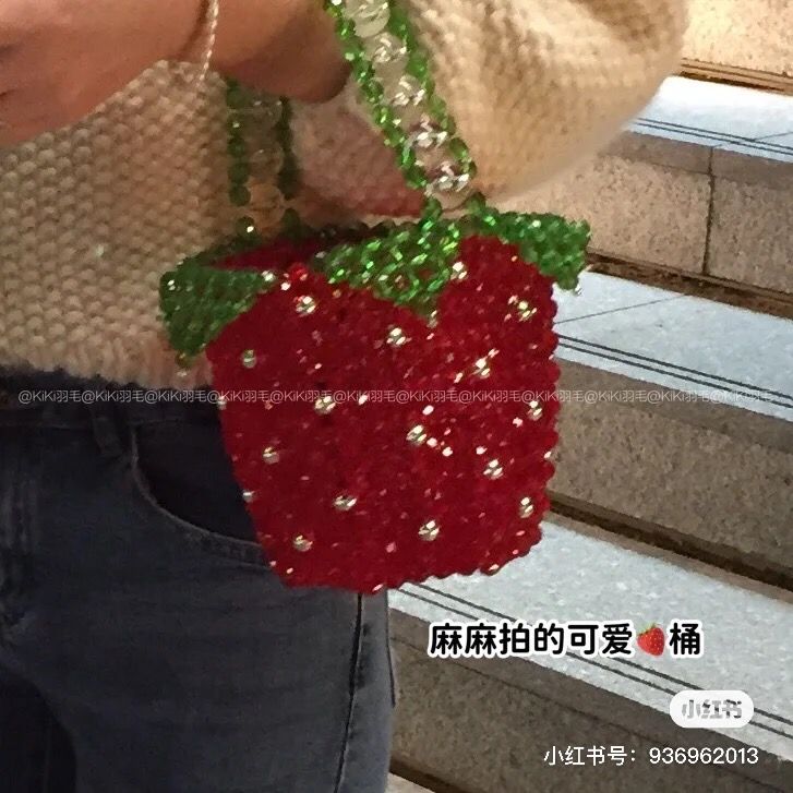 a woman holding a strawberries purse with sequins on the bottom and an attached chain