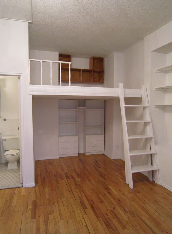 an empty room with wooden floors and white shelves on the wall, next to a ladder leading up to a toilet