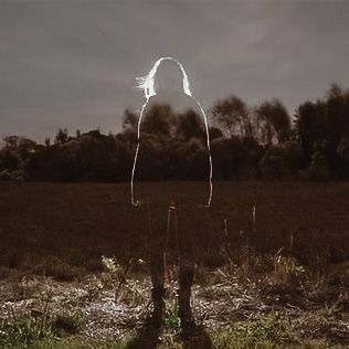 a person with long hair standing in a field under a dark sky at night time