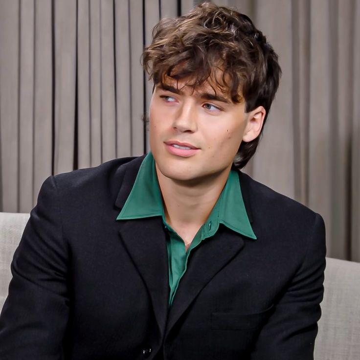 a young man sitting on top of a couch wearing a black suit and green shirt