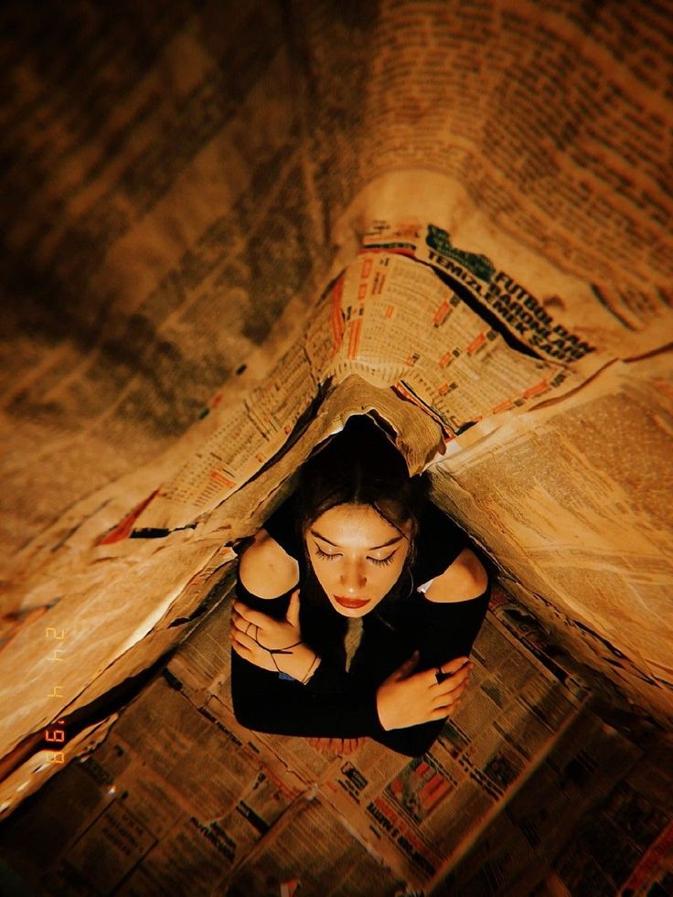 a woman laying on top of a bed covered in newspaper paper and covering her face with her hands