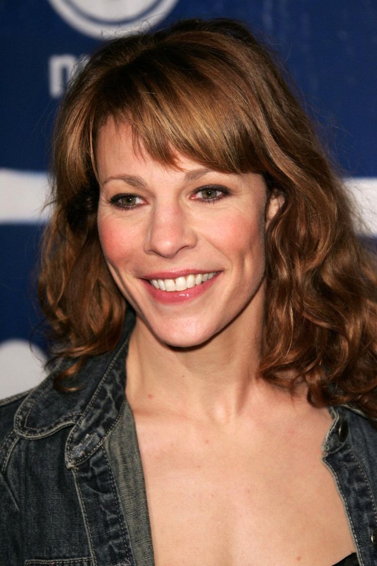 a woman with medium hair smiling at the camera and wearing a denim jacket over her shoulders