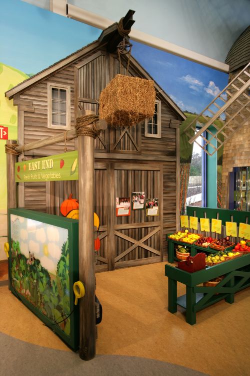 an exhibit at the children's museum displays farm animals and fruit for sale in front of a barn