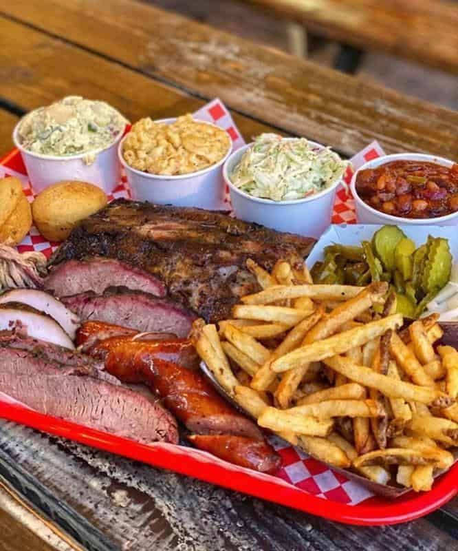 a tray filled with meat, fries and coleslaw on top of a wooden table