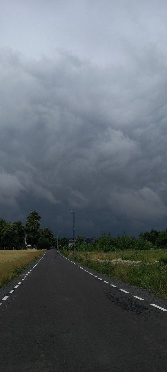 an empty road in the middle of a grassy field under a dark sky with storm clouds