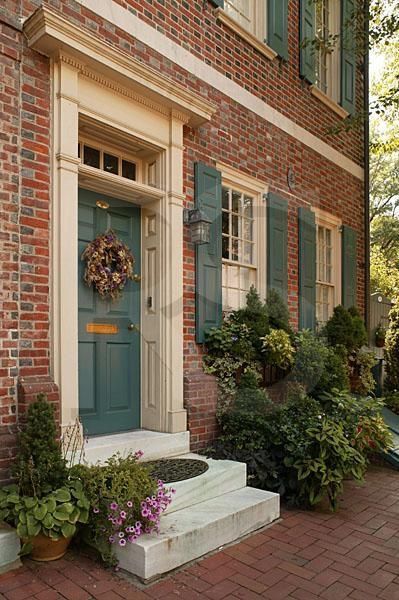 the front door of a brick house with green shutters and potted plants on either side