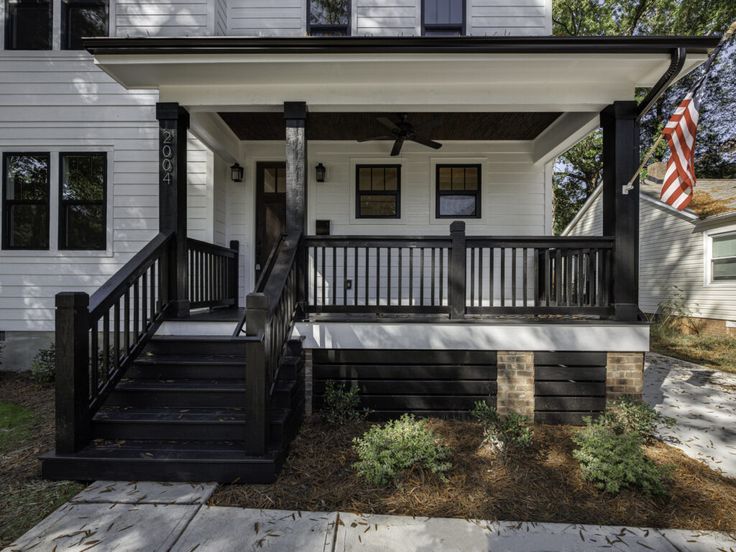 a white house with black railings and an american flag on the front door porch