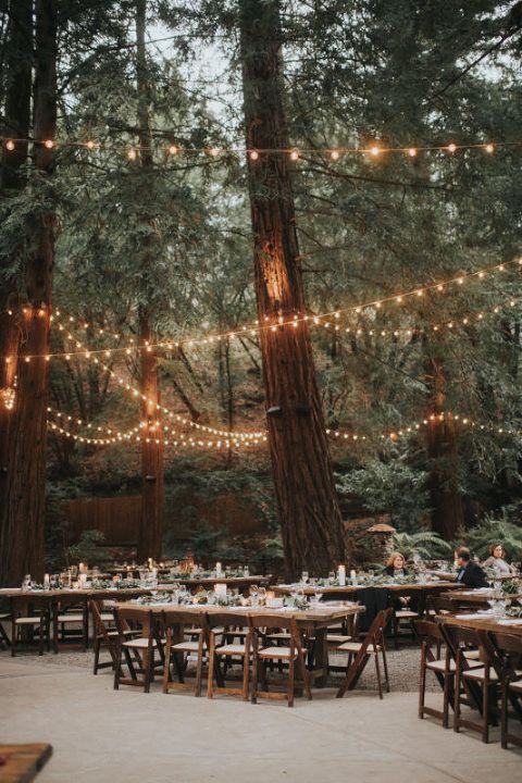 an outdoor wedding reception in the woods with string lights strung from trees and hanging over tables