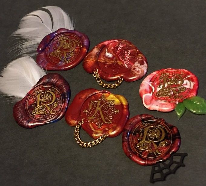 five red glass magnets with gold designs on them and a white feather laying next to it