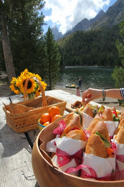 a wooden table topped with lots of sandwiches and oranges next to a body of water