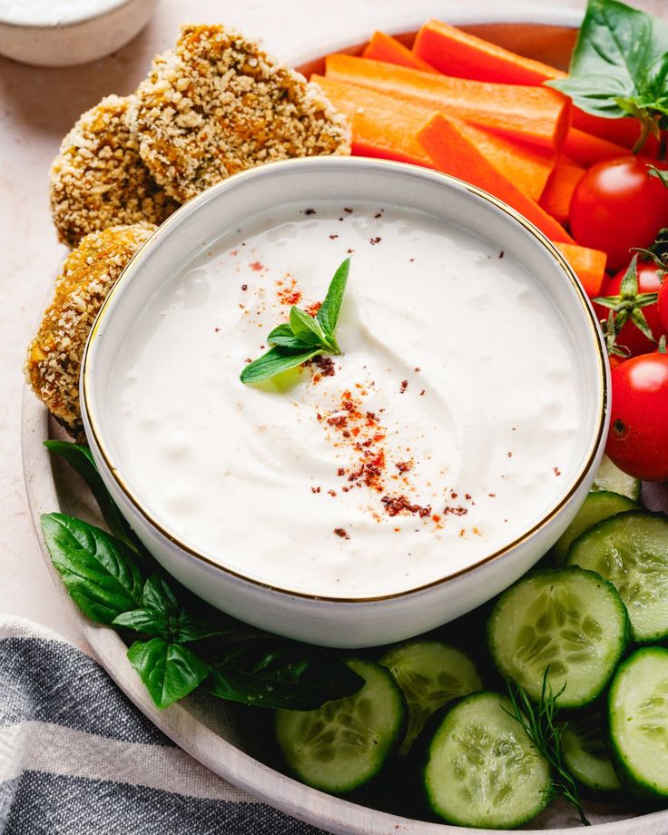 a white plate topped with cucumbers, carrots and dip