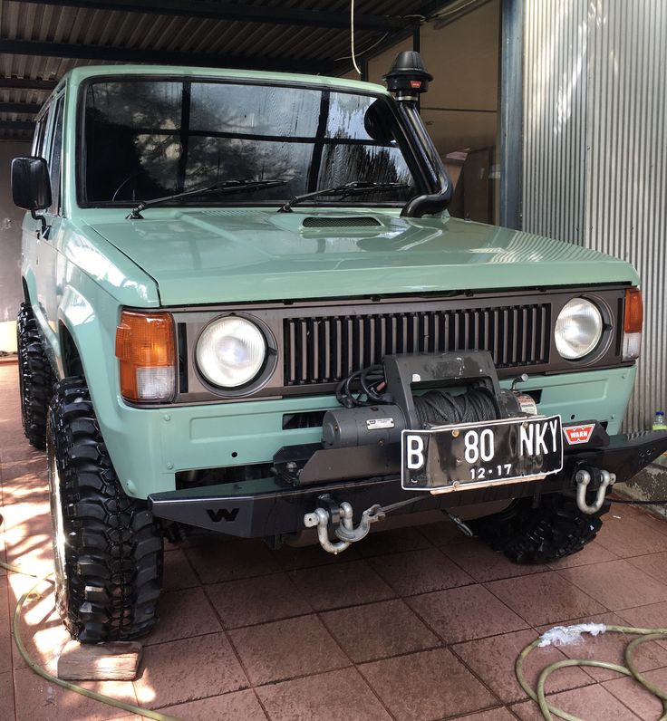 a light green truck parked in front of a building with a hose attached to it