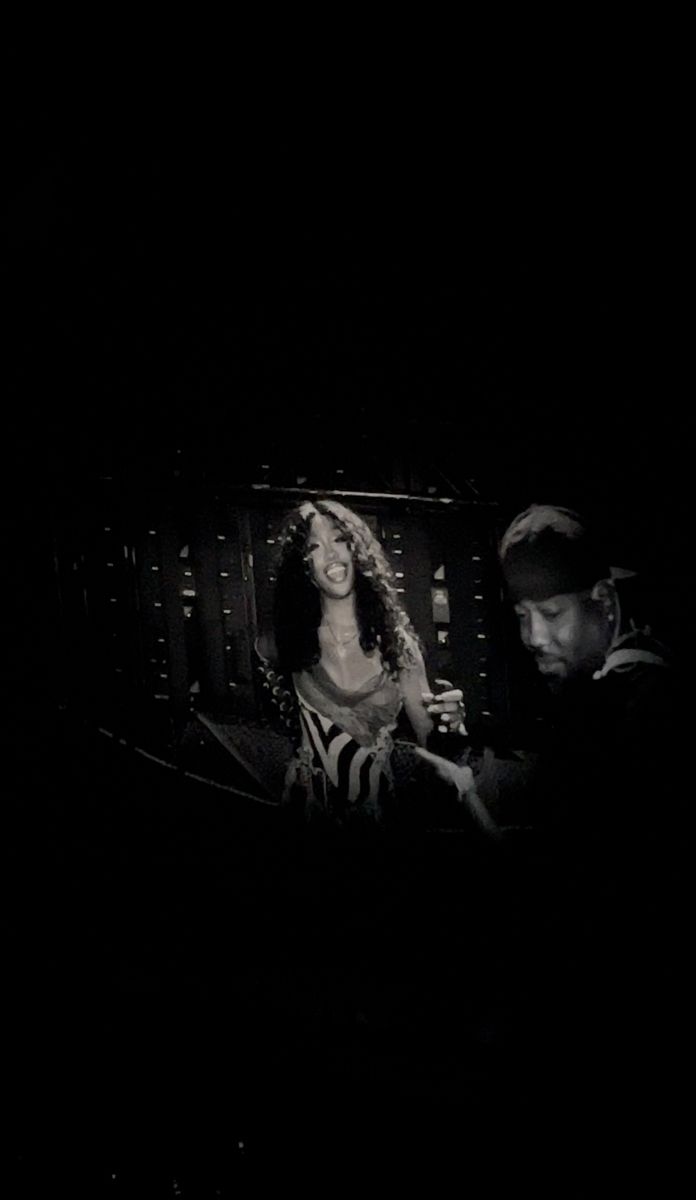 a man and woman sitting in front of a television screen at night with one person looking at the tv