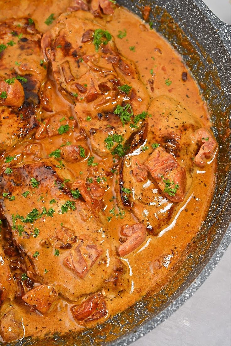 a pan filled with meat covered in gravy and garnished with parsley