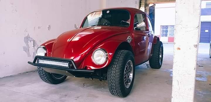 an old red car is parked in a garage next to a white wall and cement floor