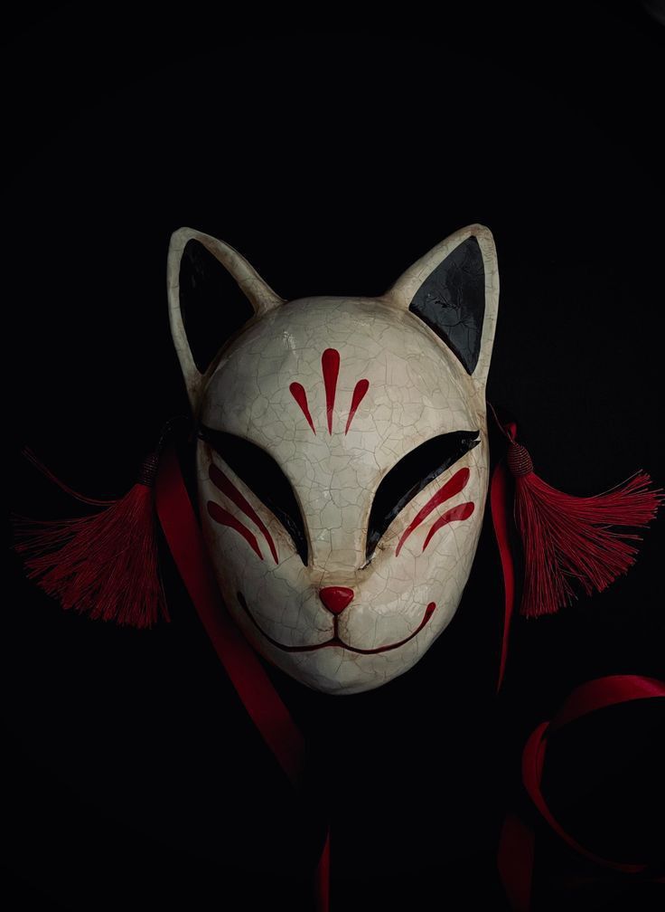 a white mask with red and black designs on it's face, sitting in the dark