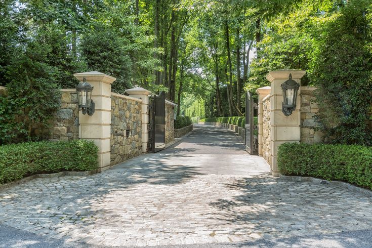 a stone driveway leading to a gated in area with trees and bushes on either side