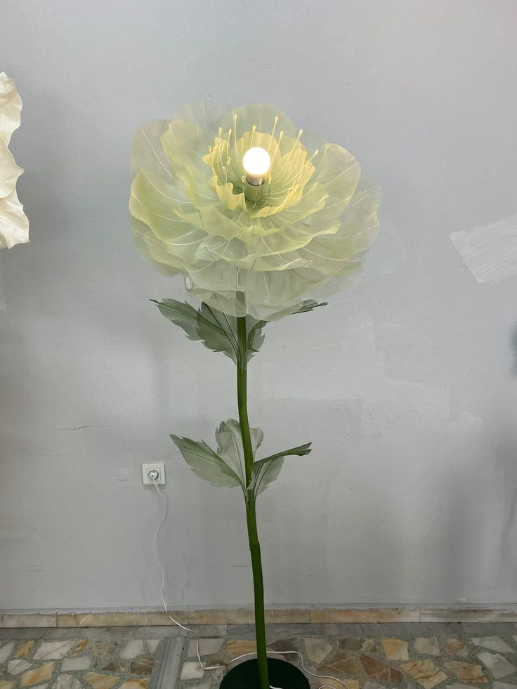 a large white flower sitting on top of a black pot next to a light bulb