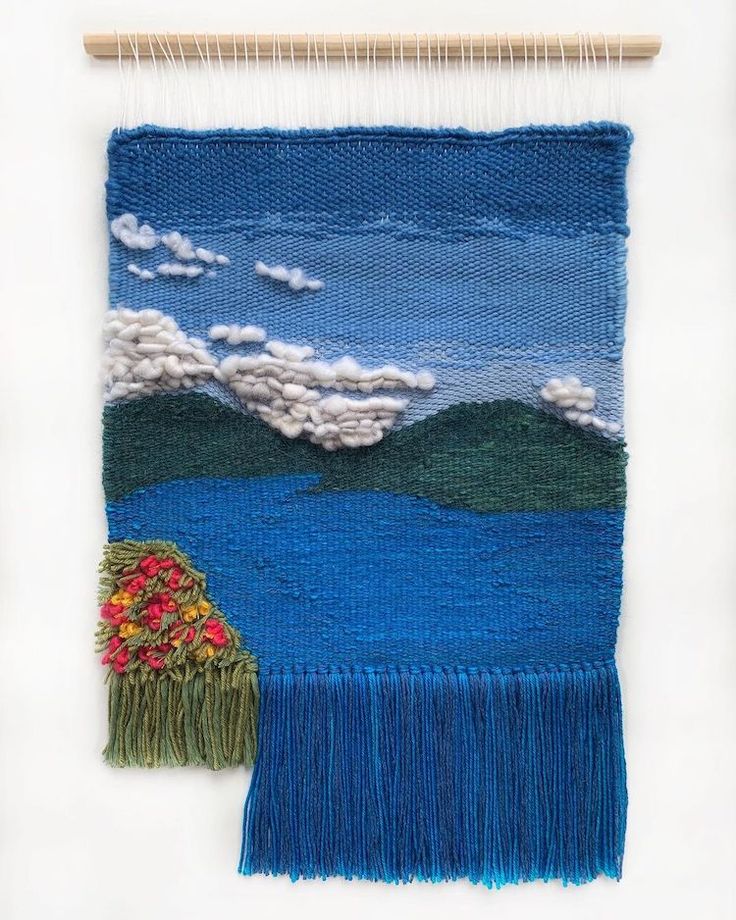 a weaving project with blue and green colors on the wall next to a piece of wood