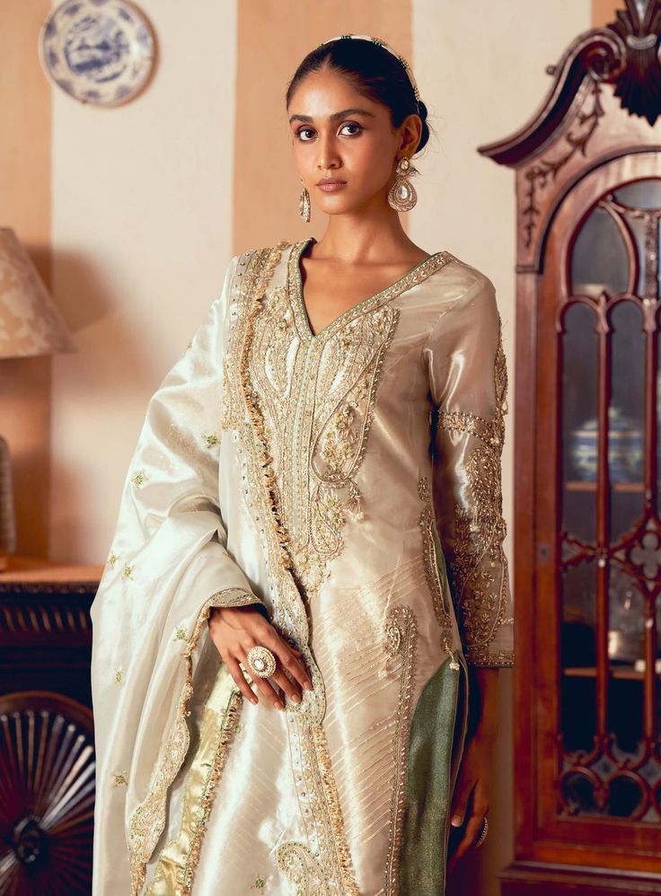 Embrace timeless sophistication with this classic kurti set, meticulously crafted from pearl gold silk zari tissue and jacquard silk banarasi. The design features jharokha-inspired panels, intricately embroidered with elongated paisley patterns in zari and zardozi work, enhanced with dabka, sequins, and pearls for added depth and richness. Complementing the look is a shimmering pearl gold tissue dupatta adorned with matching jharokha-inspired panels and pearl detailing. The straight pants, crafted from soft silk and showcasing gota texturing at the hem, create a gracefully defined and elegant silhouette. Tissue Kurta, Tissue Dupatta, Zardozi Work, Kurti Set, Gold Silk, Kurta Set, Paisley Pattern, Straight Pants, Design Features