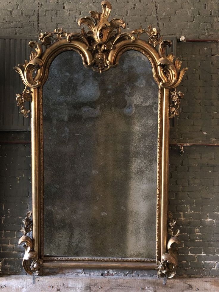 an ornate gold framed mirror against a brick wall