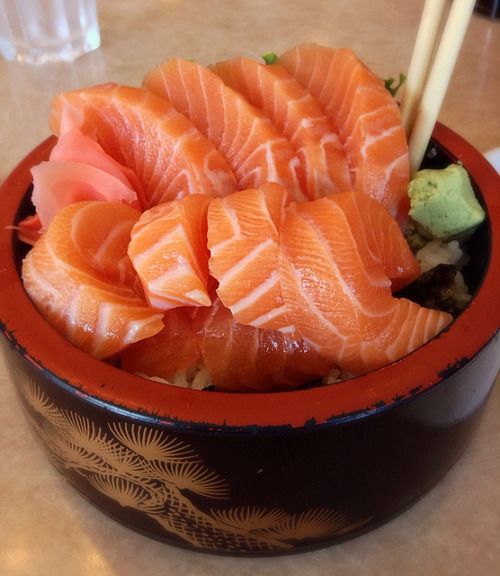 a bowl filled with salmon and sushi on top of a table