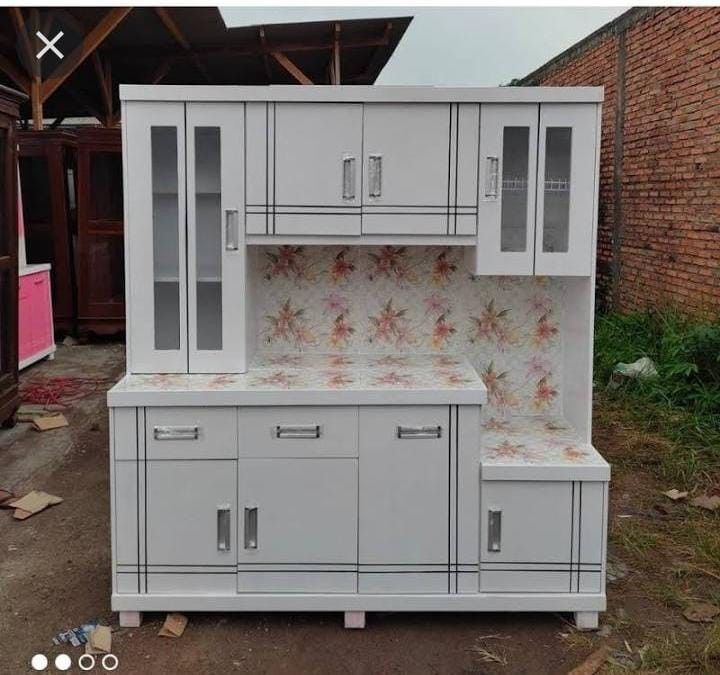 a white kitchen cabinet sitting on top of a dirt ground next to a brick wall