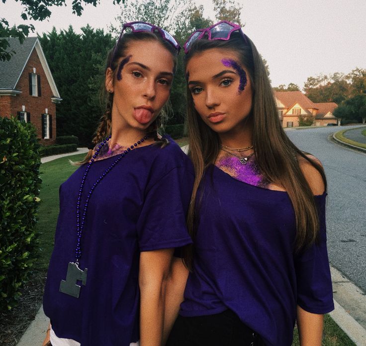 two young women standing next to each other in front of a house with purple paint on their faces