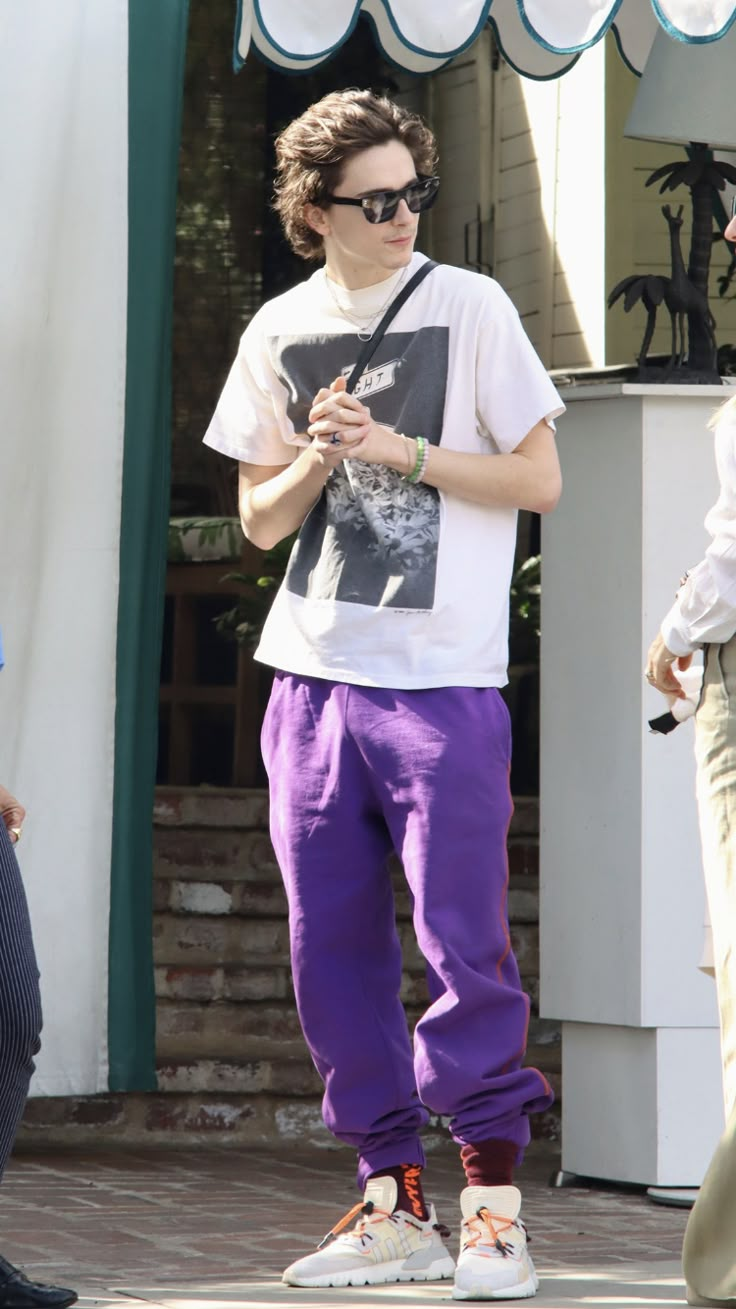 a young man wearing purple pants and a t - shirt is looking at his cell phone