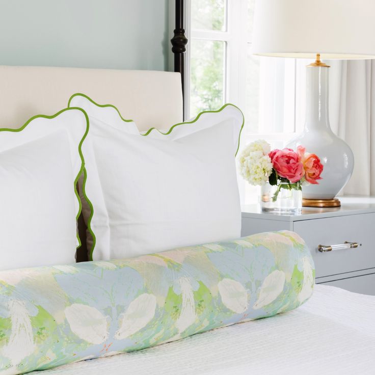 a bed with white pillows and green trim on it, next to a nightstand with flowers