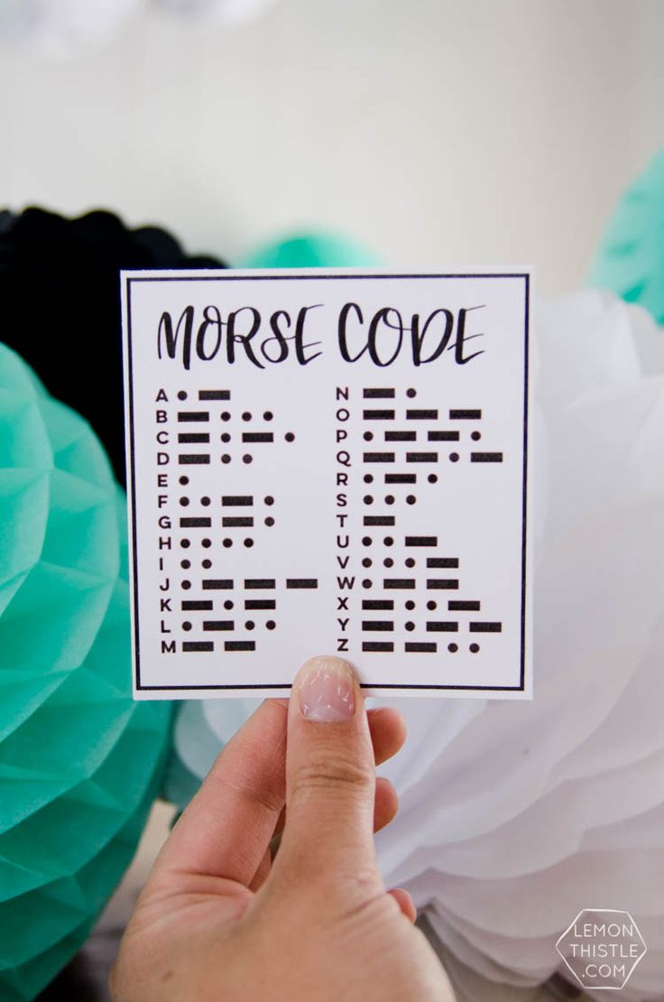 someone holding up a morse code card in front of some paper balls and tissue pom poms