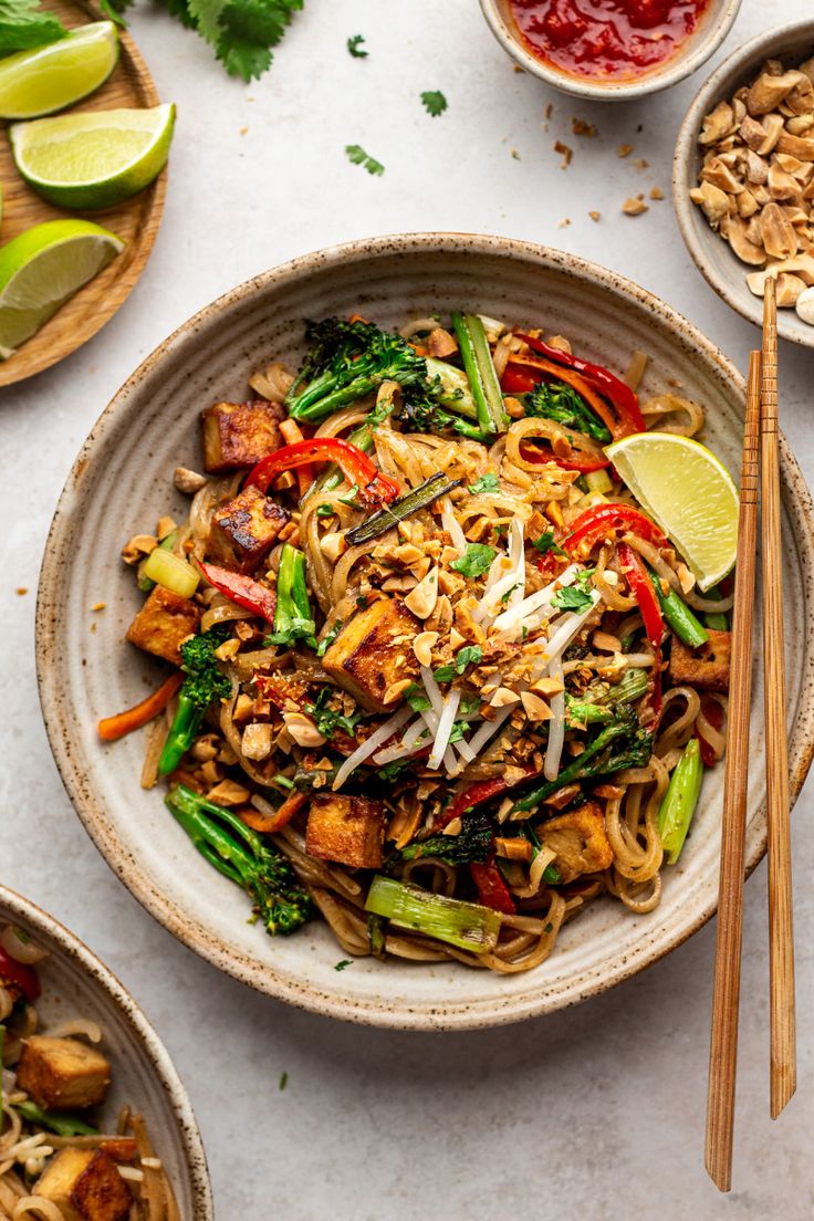 a bowl filled with noodles and vegetables next to chopsticks on a table top