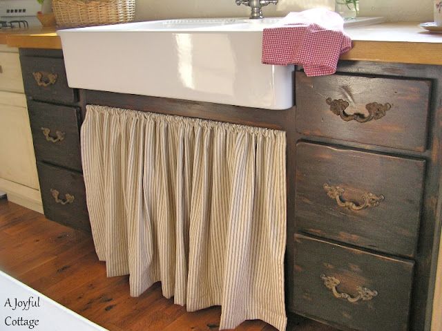 a kitchen sink and counter with curtains on it