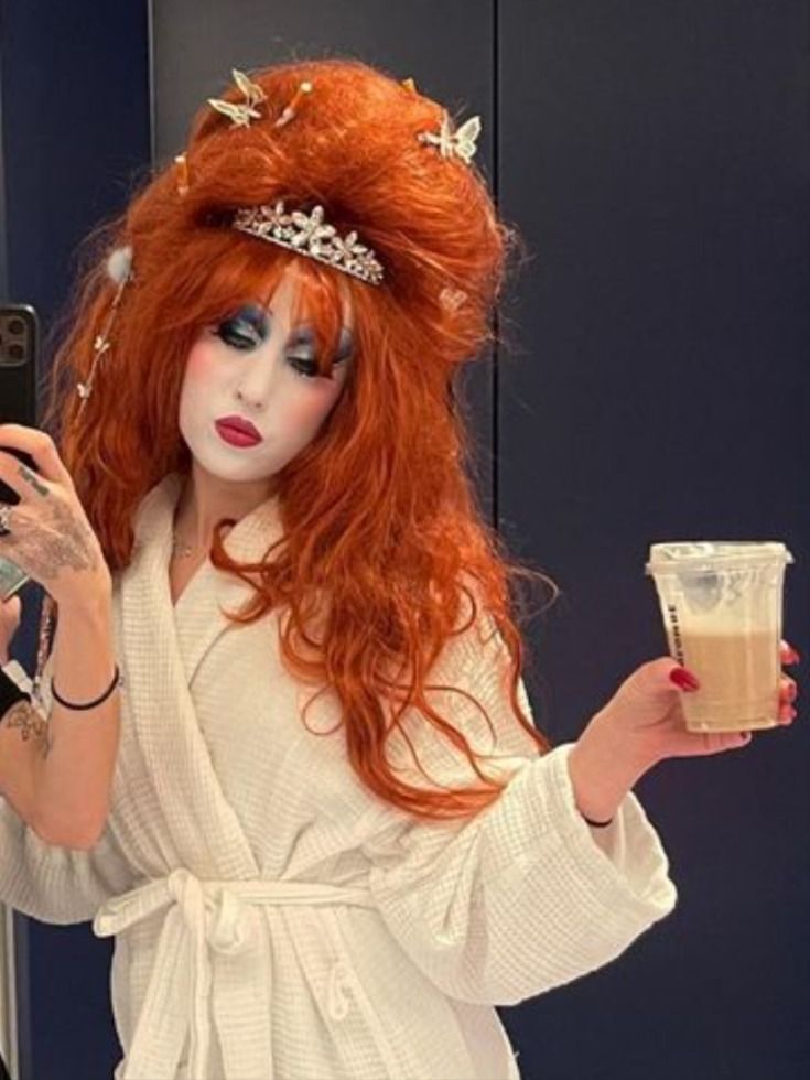 a woman with red hair is taking a selfie in front of a mirror and holding a drink