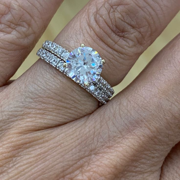 a woman's hand with a diamond ring on top of her wedding band and an engagement ring in the middle