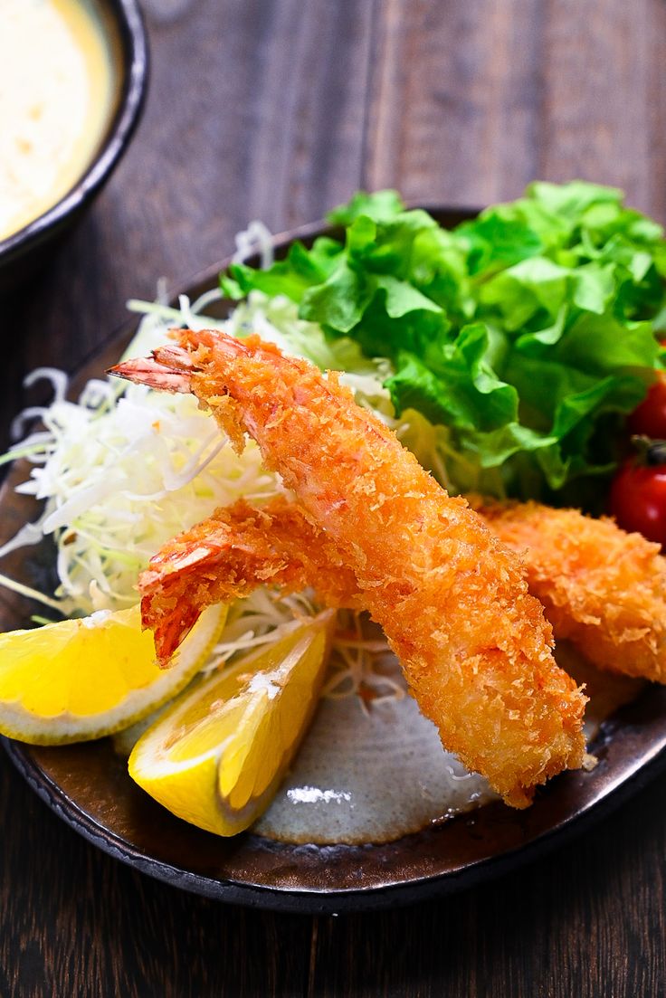 a plate with shrimp, lettuce and lemon wedges next to a bowl of dip