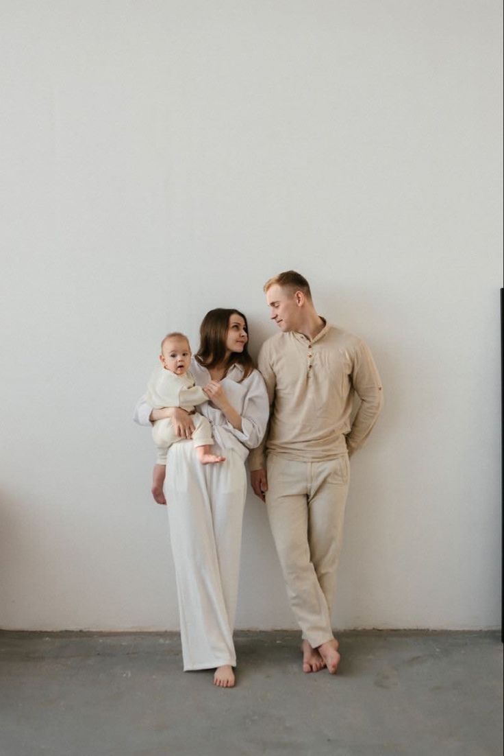 a family standing next to each other in front of a white wall and holding their baby