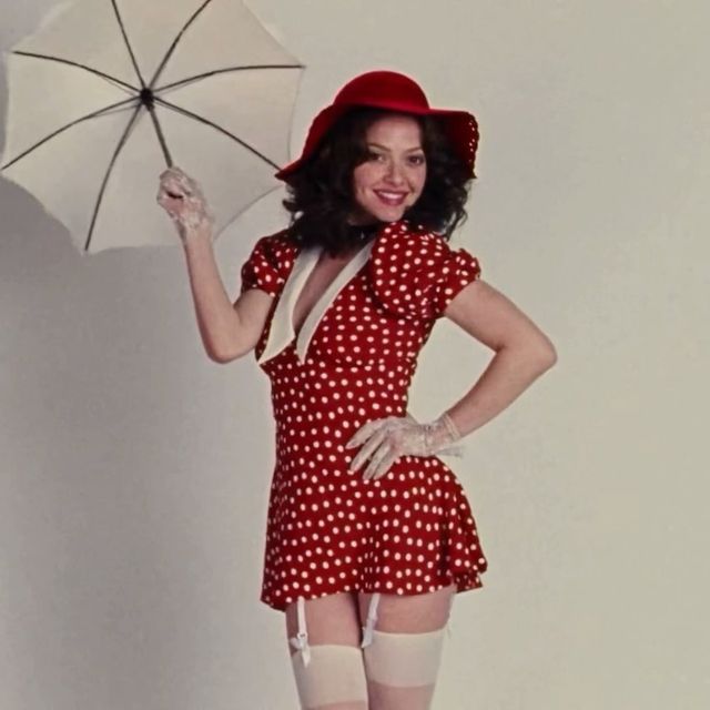 a woman in a red polka dot dress and white stockings holding an umbrella over her head