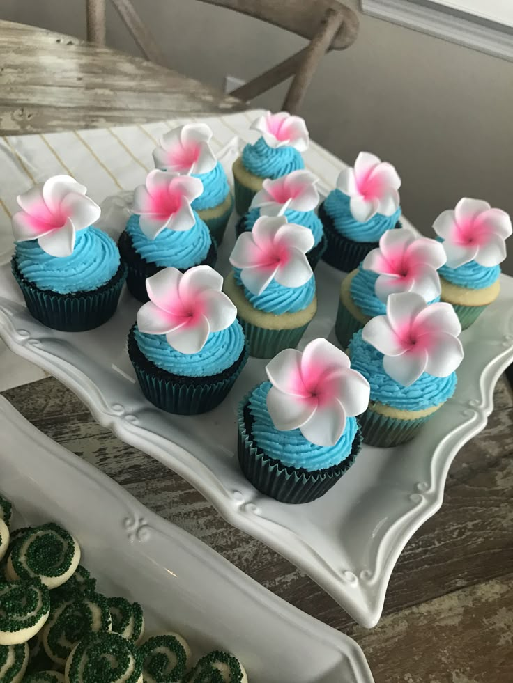 cupcakes with blue frosting and pink flowers on them sitting on a plate