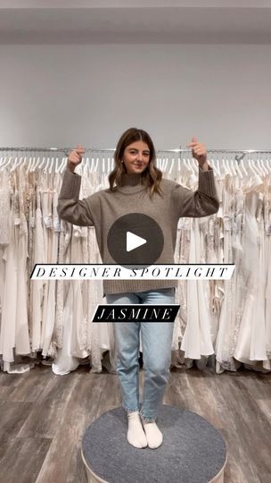 a woman is standing in front of a rack of dresses and holding her hands up