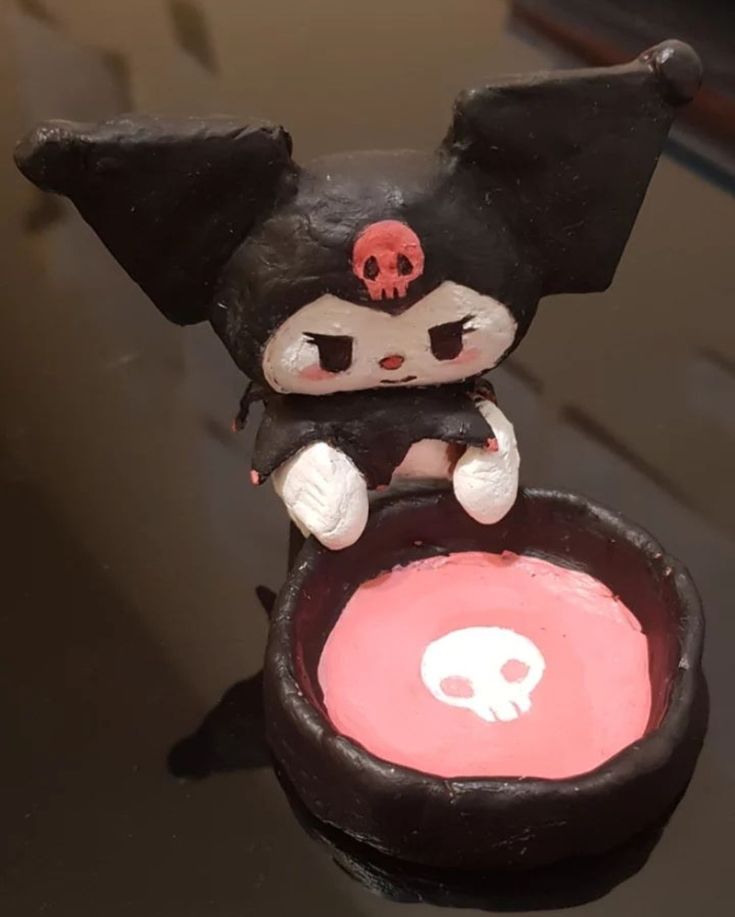 a cat figurine sitting on top of a black container with a skull in it