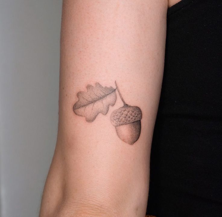 a woman's arm with a tattoo on it that has leaves and acorns