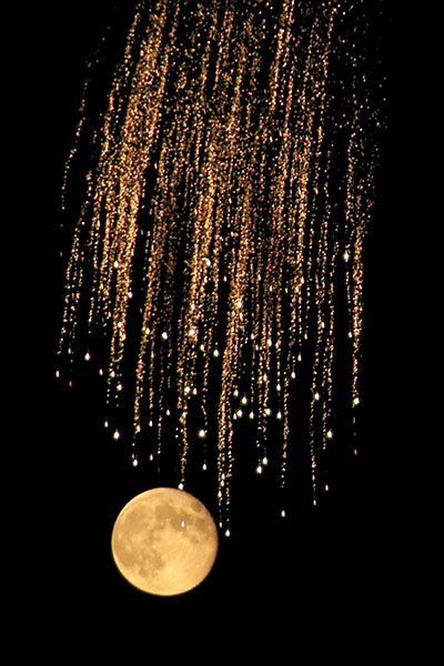 the moon is shining brightly in the night sky with rain falling from it's branches