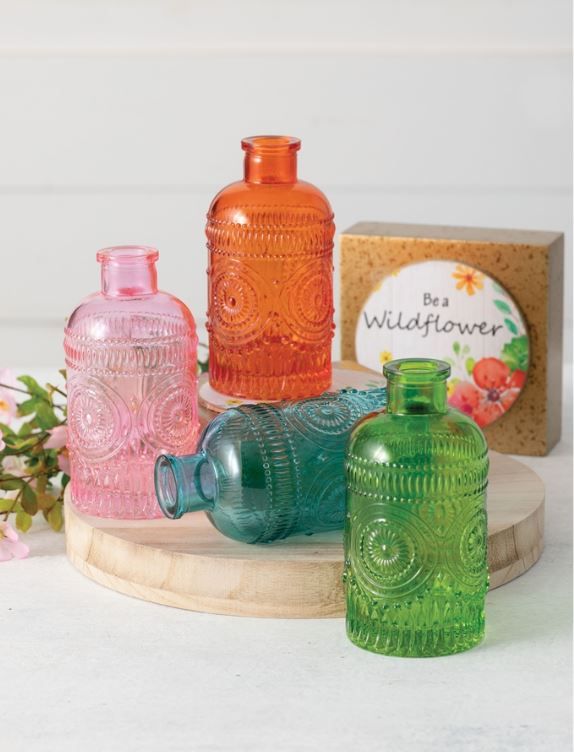 three colorful glass bottles sitting on top of a wooden board next to flowers and a box