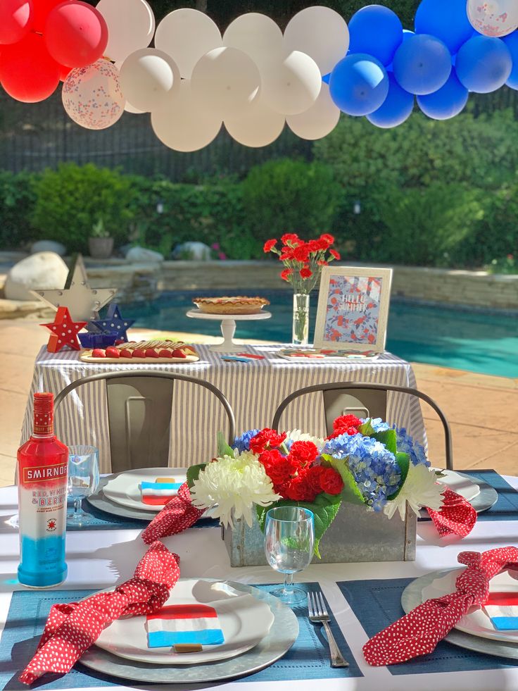 a table set up with plates, silverware and red white and blue balloons hanging from the ceiling