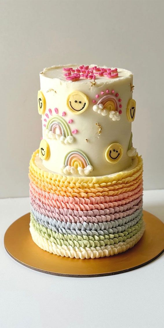 a multicolored cake with smiley faces and rainbows on the top is sitting on a plate