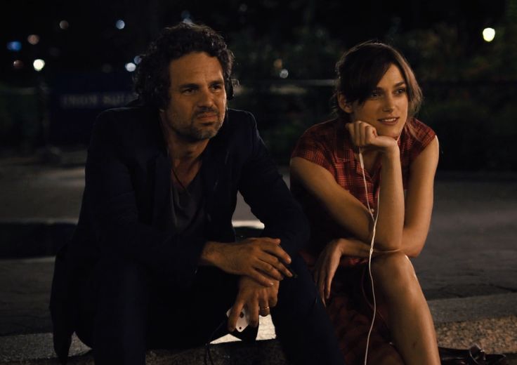 a man sitting next to a woman on top of a sidewalk at night with headphones in her ears